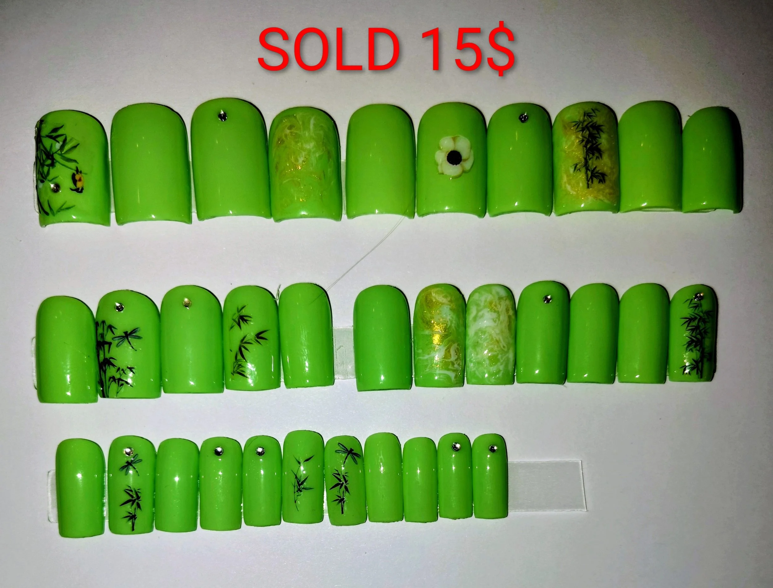 A set of decorative green false nails with floral and bamboo designs. The nails are arranged in two rows on a white background, with red text above them that reads 'SOLD 15$'.
