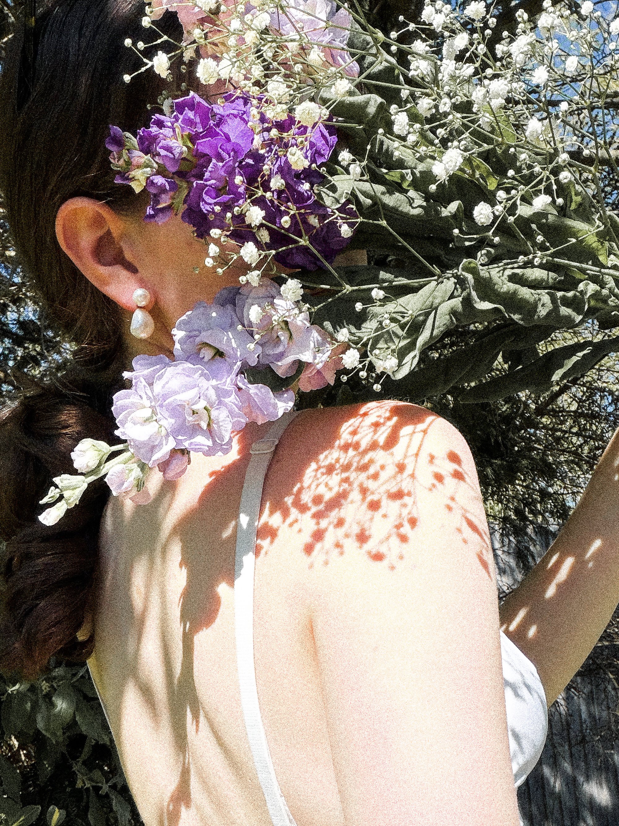 Woman holding a bouquet of purple flowers over her shoulder highlighting a visible bra strap.