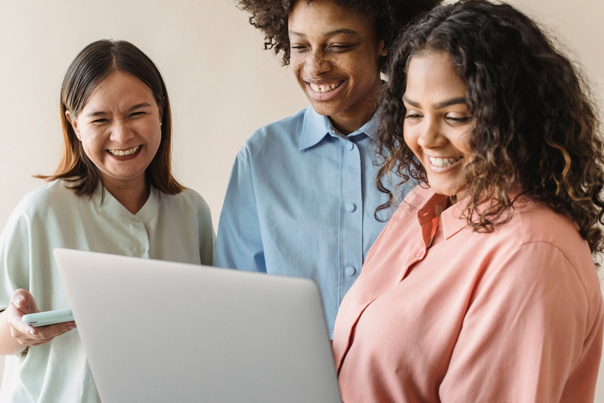 Three women are looking at a laptop screen and smiling, suggesting a positive and collaborative atmosphere.