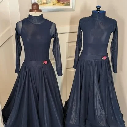 Two dark blue mannequins wearing matching long-sleeved, high-neck dresses with pleated skirts, displayed in a store.