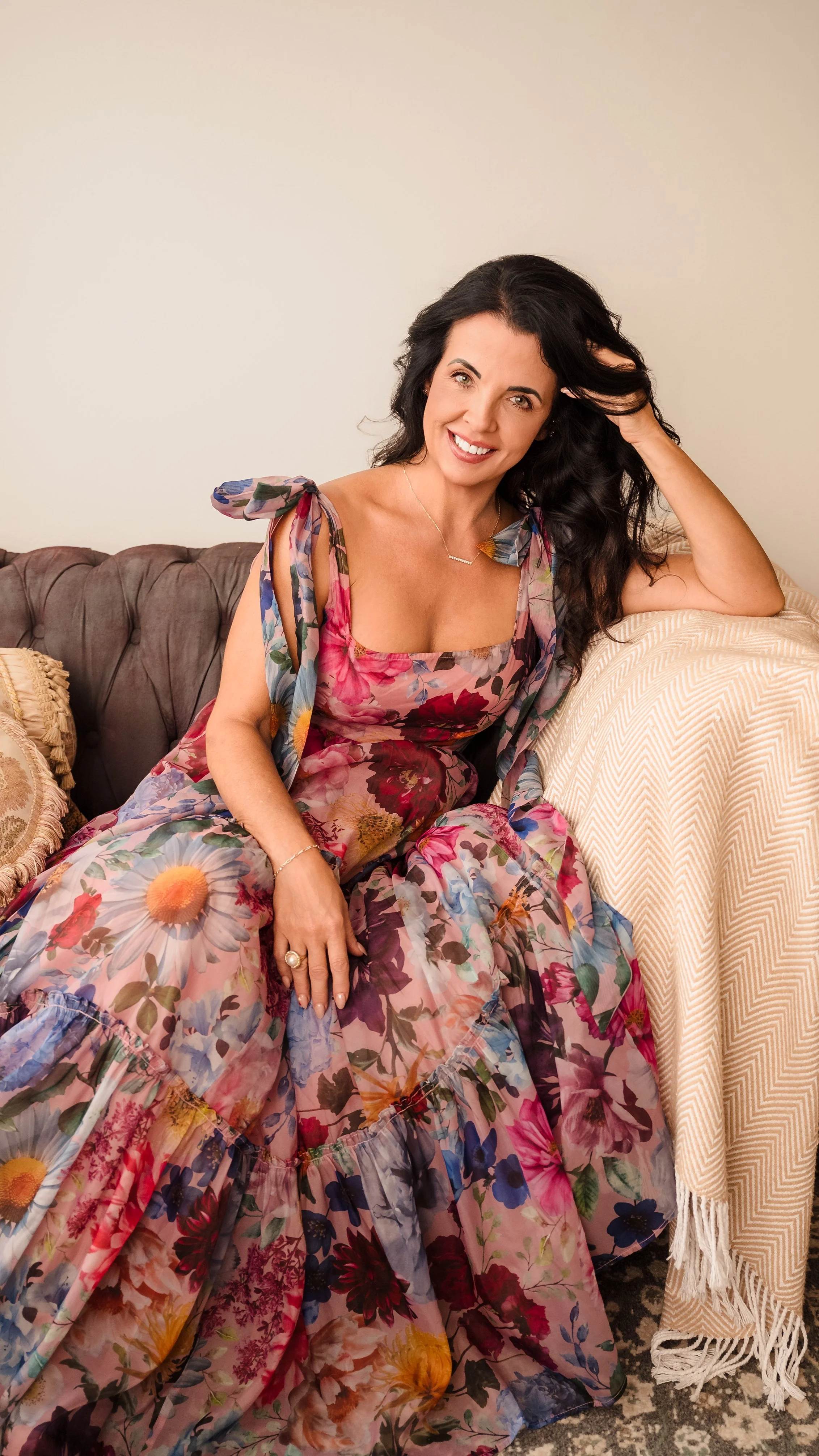 Vanessa Sexton seated on a styled sofa while wearing a colorful floral dress.