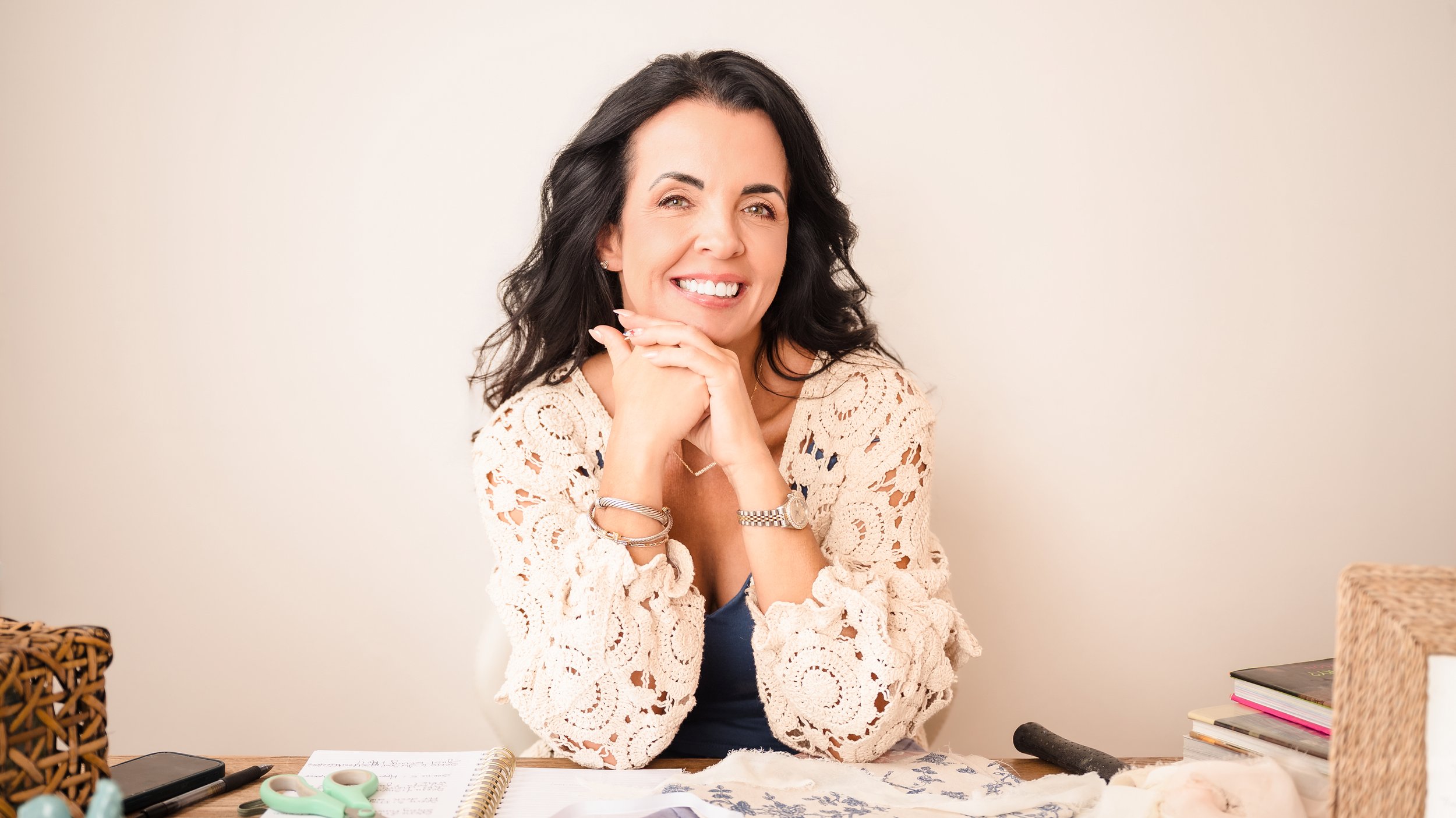 Vanessa Sexton smiling at a creative workspace with fabric samples, notebooks, and styling materials.
