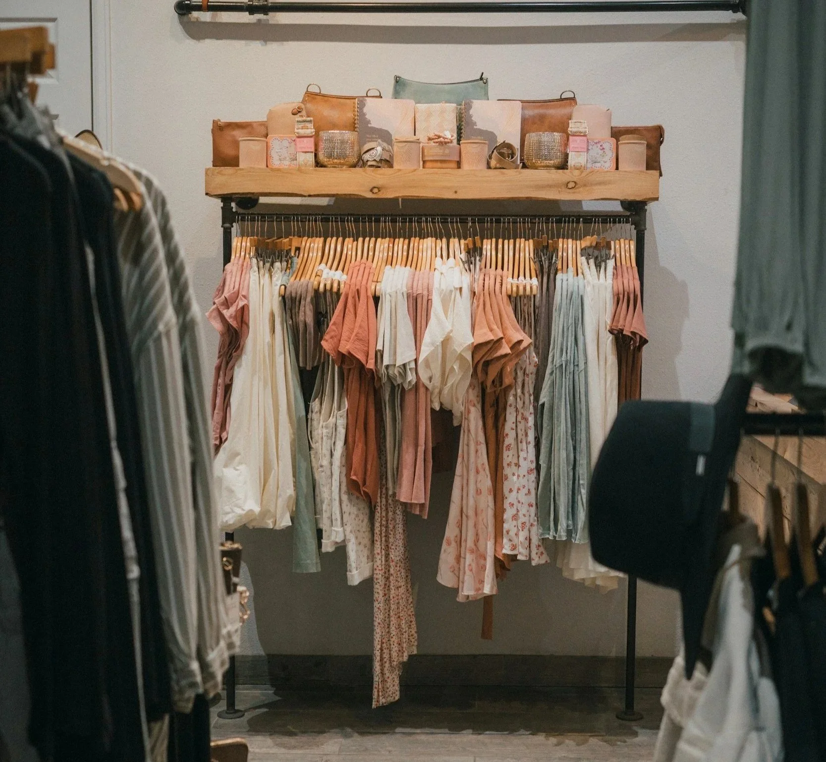 A clothing display in a store with various pastel-colored dresses hanging on a rack and decorative items on a wooden shelf above.