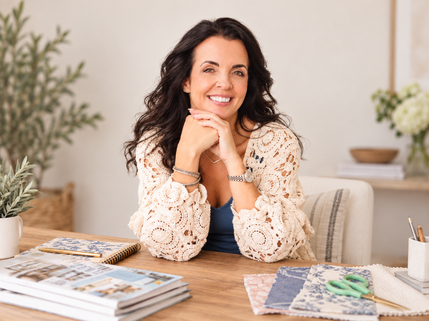 Vanessa Sexton smiling at a table with fabric, scissors, magazines, and styling materials in a bright, cozy workspace.