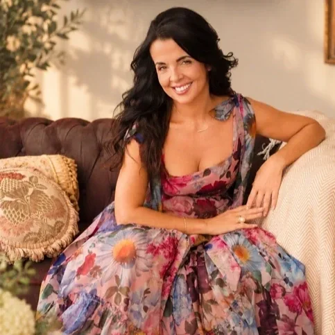 Vanessa Sexton seated on a sofa in a colorful floral dress, reflecting her warm and creative styling personality.