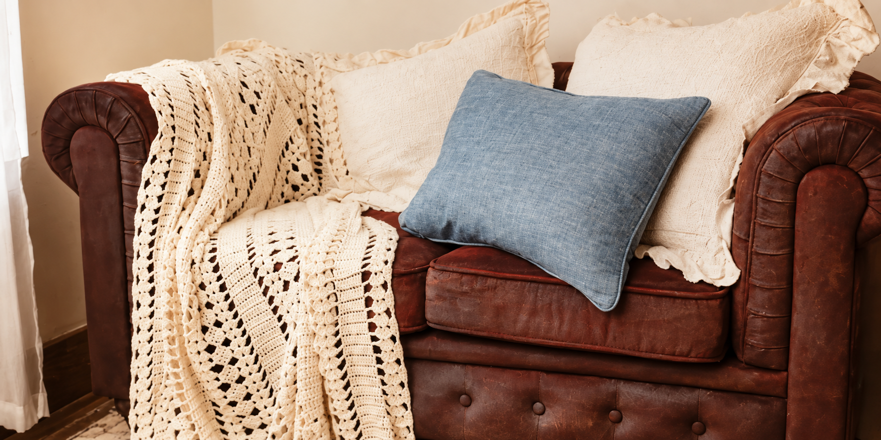 Brown leather sofa layered with cream pillows, a dusty blue cushion, and an ivory crocheted throw.