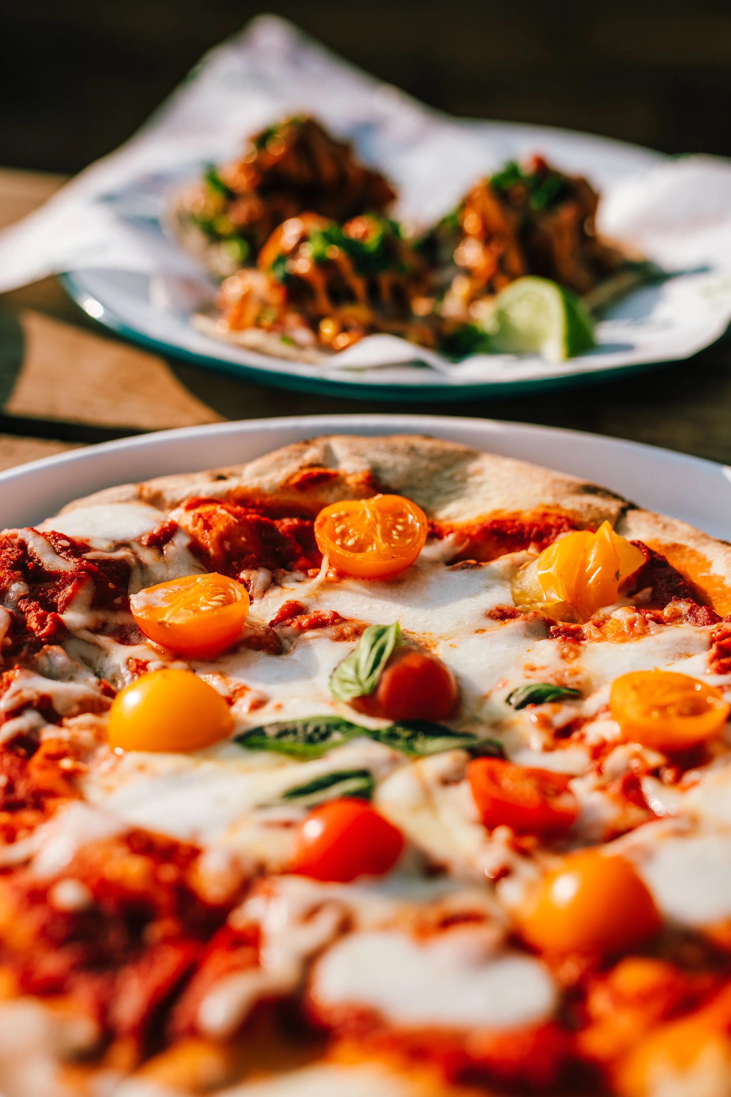 Close-up of a pizza with cherry tomatoes, basil, melted cheese, and pepperoni.
