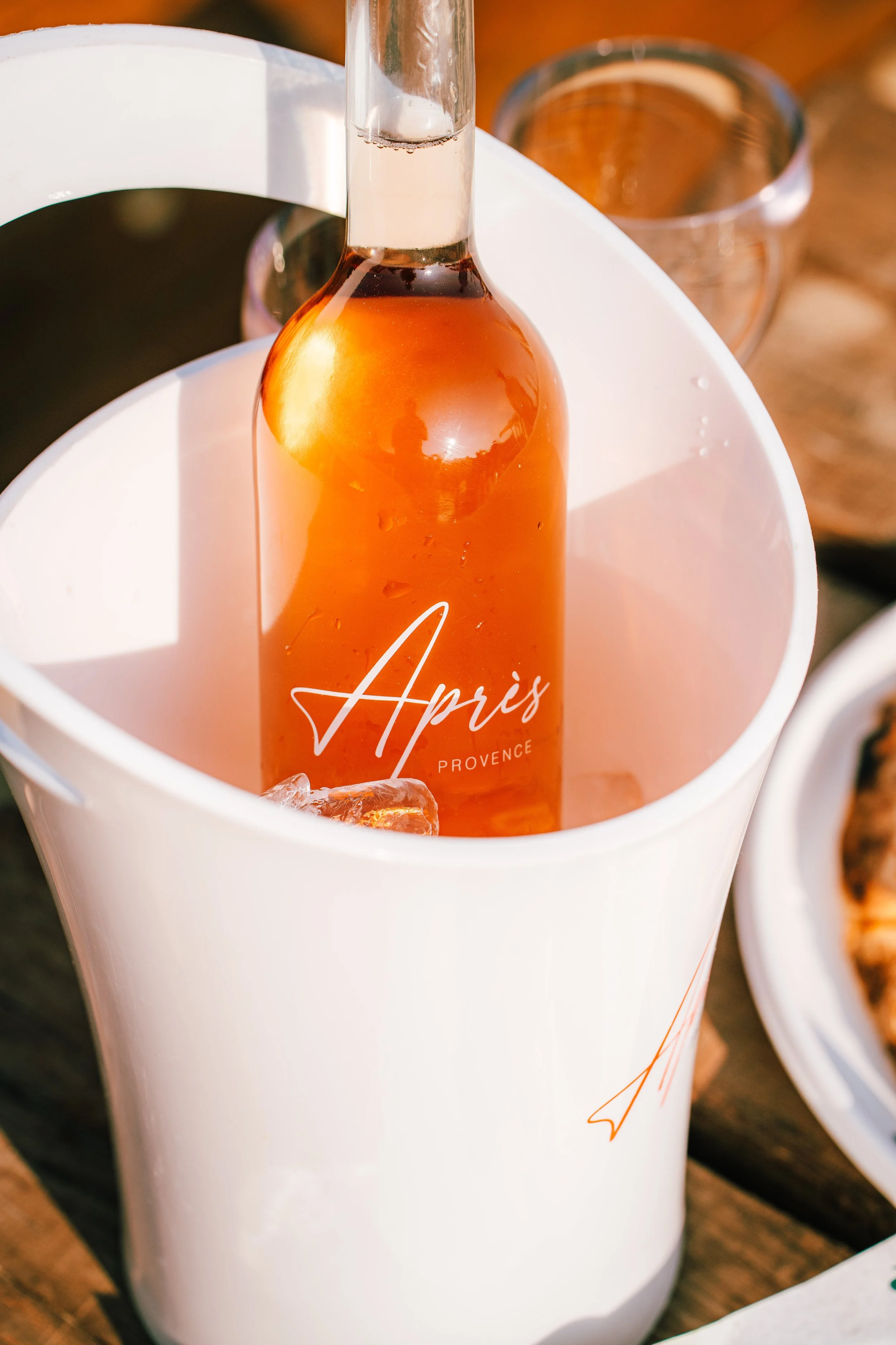 A bottle of Apris Provence rosé wine in an ice bucket with ice cubes, set outdoors.