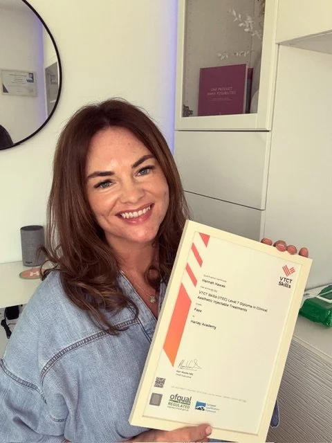 A woman with brown hair smiling and holding a certificate in a medical or professional setting.