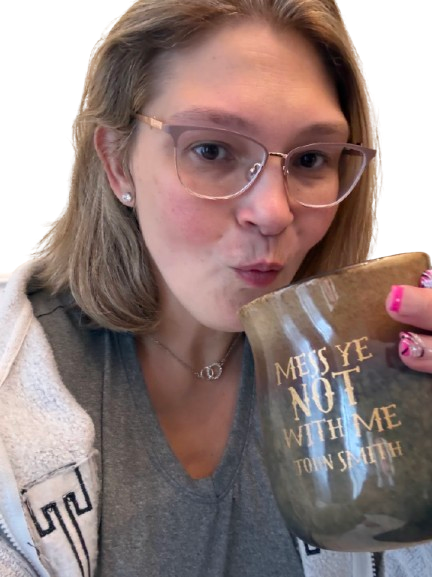 Woman with glasses holding and about to sip from a mug that says "YES, I'LL NOTE WITH ME"
