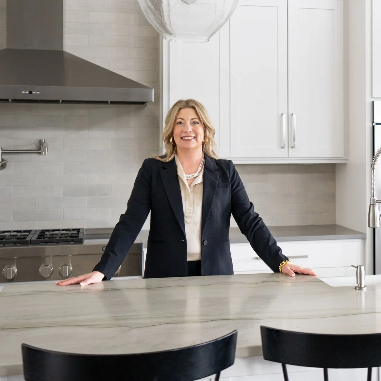 Jenny Quirie, licensed Oregon Realtor, Seniors Real Estate Specialist, and certified Safe Home Specialist, founder of Forever Home Senior Advisors, smiling in a bright modern kitchen wearing a black blazer.