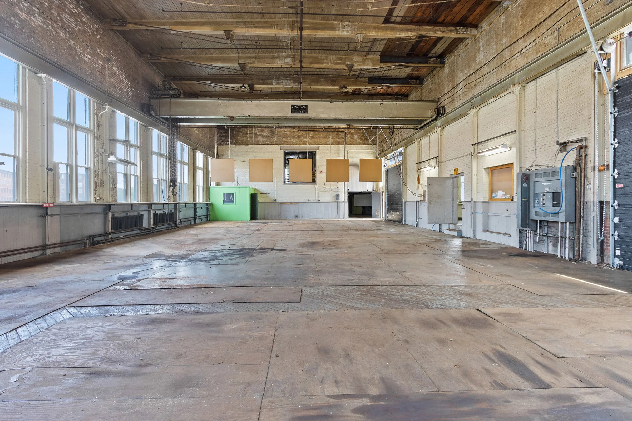 Empty industrial space with large windows, wooden ceiling, and exposed pipes and electrical systems.