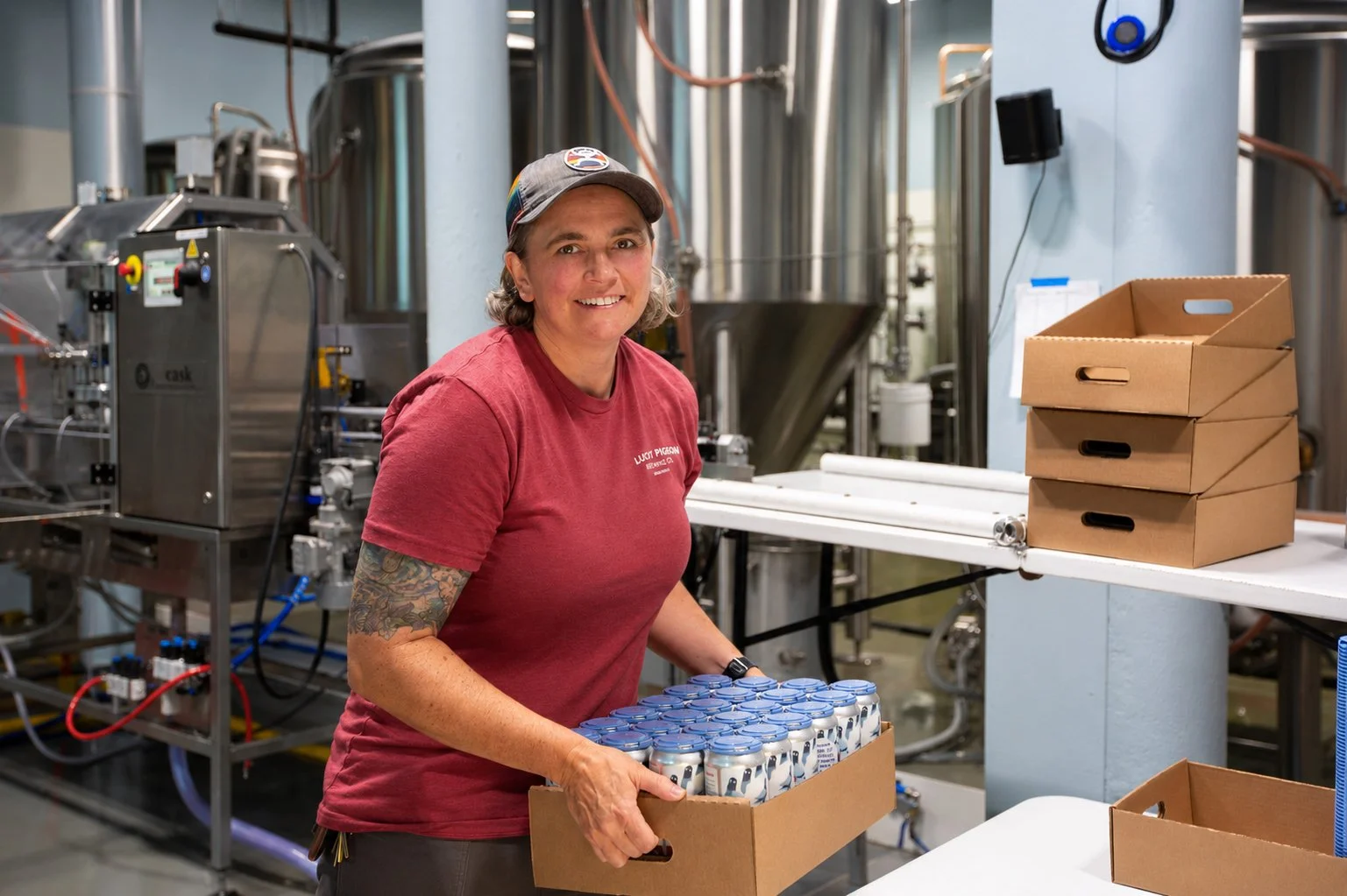 A woman in a red t-shirt holding a box of beers at Lucky Pidgeon Brewery.