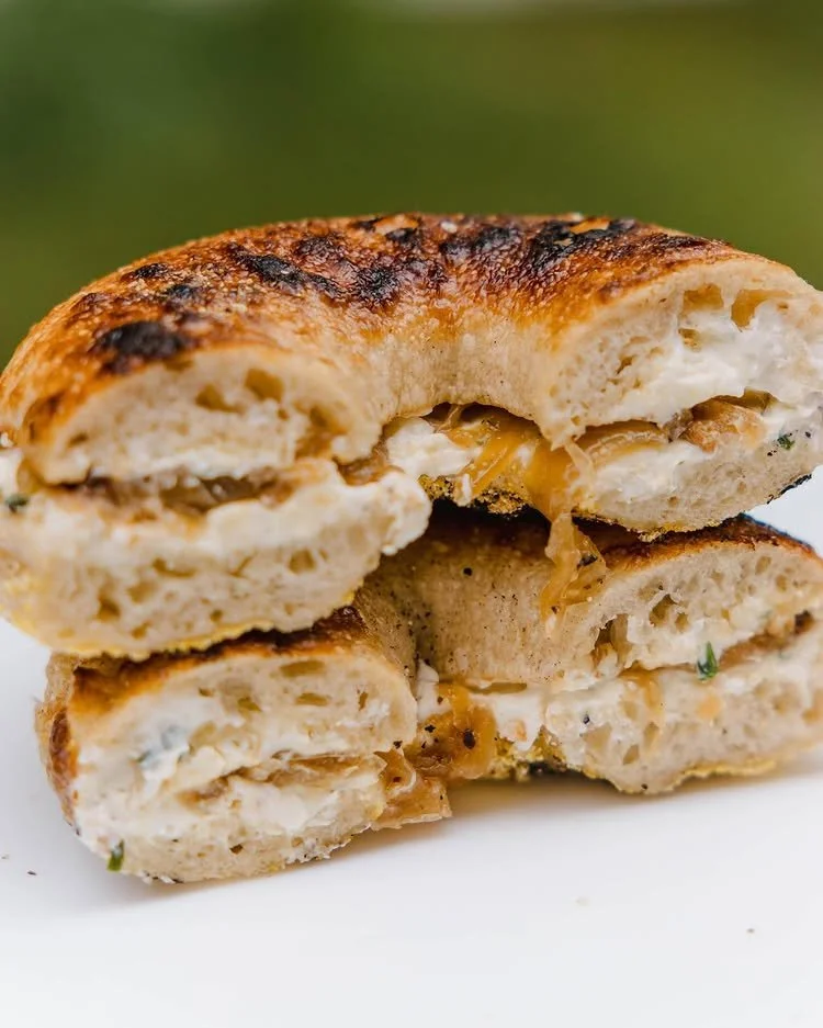 Close-up of a bagel sandwich from Rover Bagels cut in half on a white plate with a blurred outdoor background.