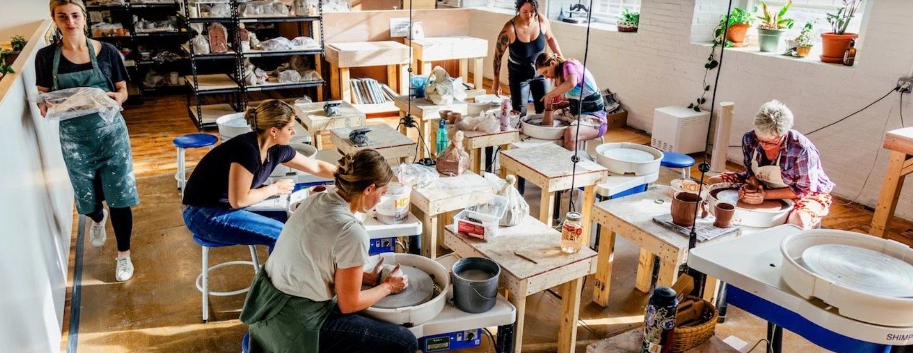 People participating in a pottery class working on pottery wheels in a well-lit studio.