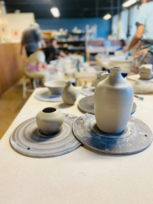 Clay pottery in a pottery studio with people working in the background.