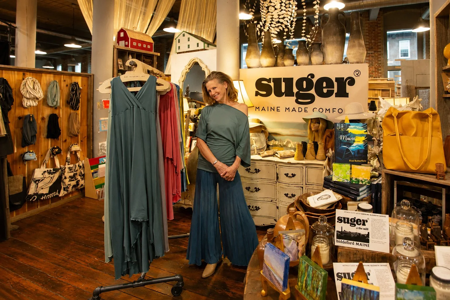 A woman shopping inside a boutique store called 'Suger' in Biddeford, Maine, surrounded by clothing, books, and decorative items.