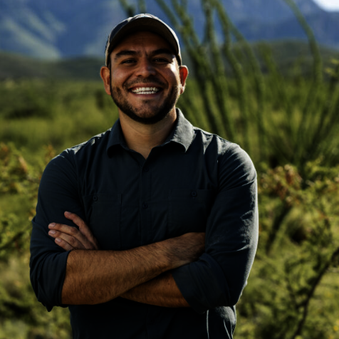 Man smiling outdoors in front of a green landscape with mountains.