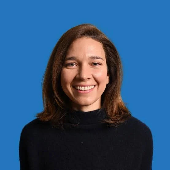 Headshot of Rebecca Bennett, young women in black turtleneck against a bright blue background