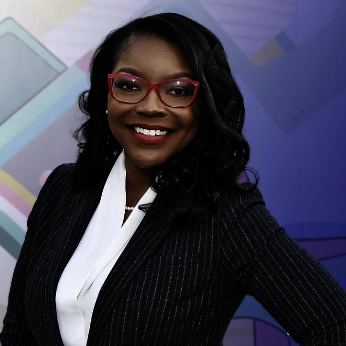 Professional woman with curly black hair, wearing red glasses, a pinstripe blazer, white blouse, and a pearl necklace, smiling in front of a colorful background.