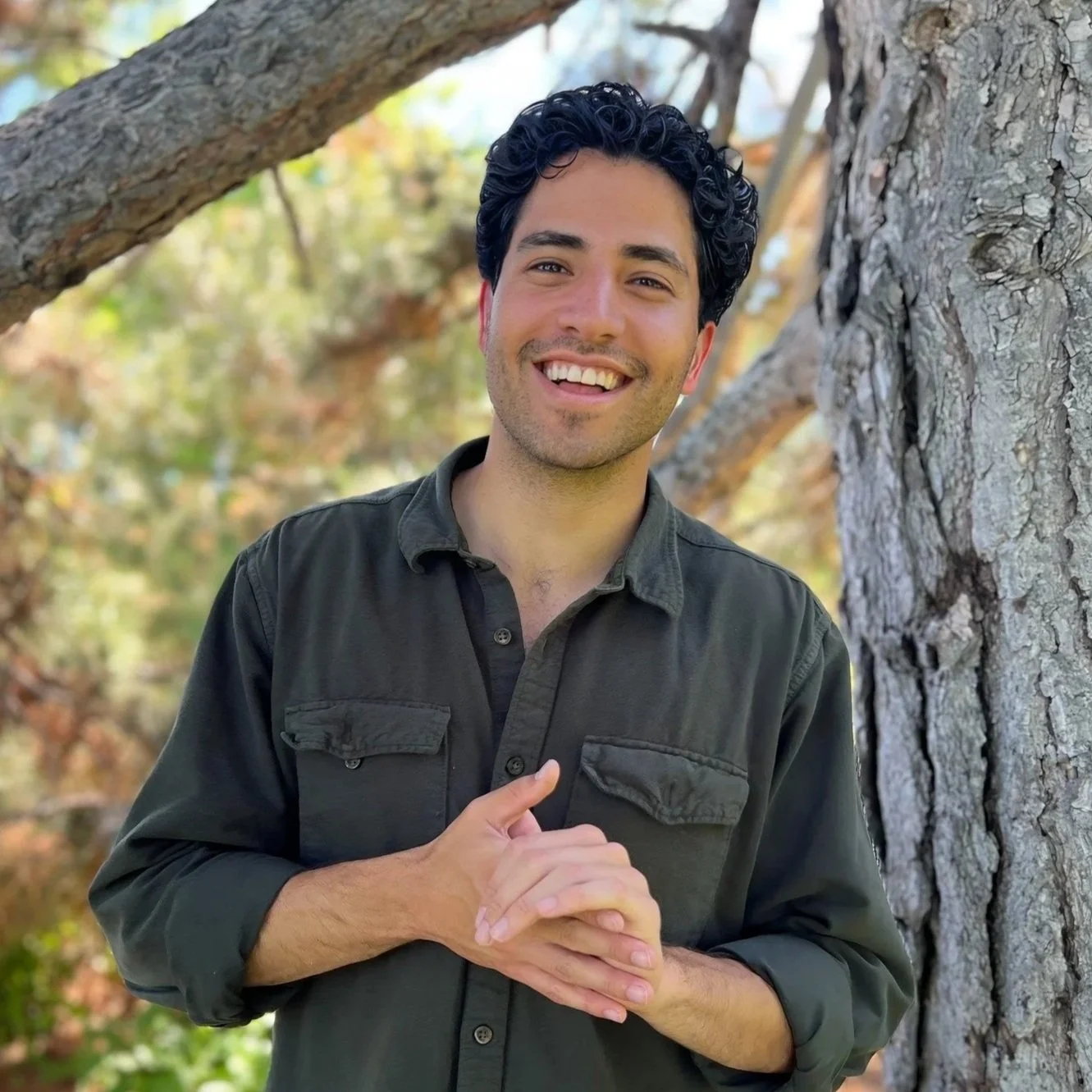 Headshot of Manny Rutinel outdoors next to a tree smiling towards the camera