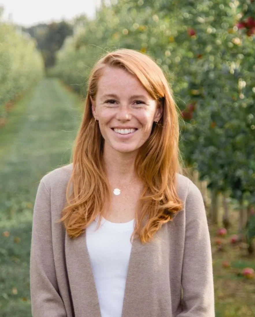 Headshot of Rebecca Cooke standing in an orchard smiling