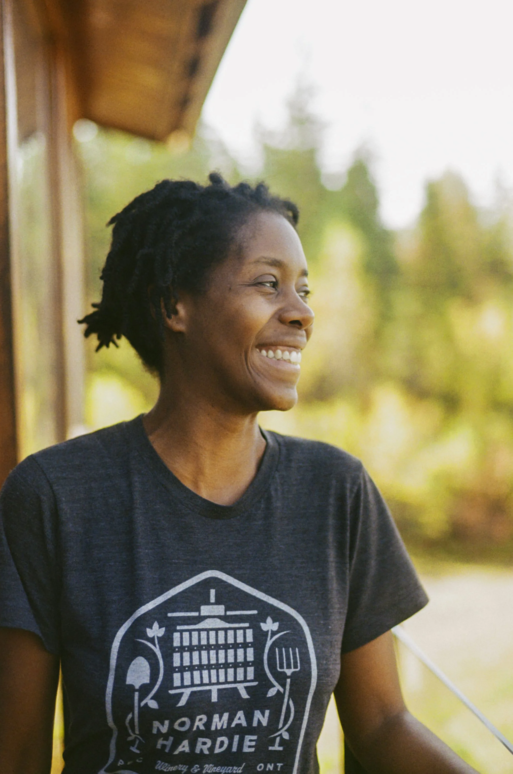 A woman smiling outdoors wearing a dark T-shirt with a graphic and text design.