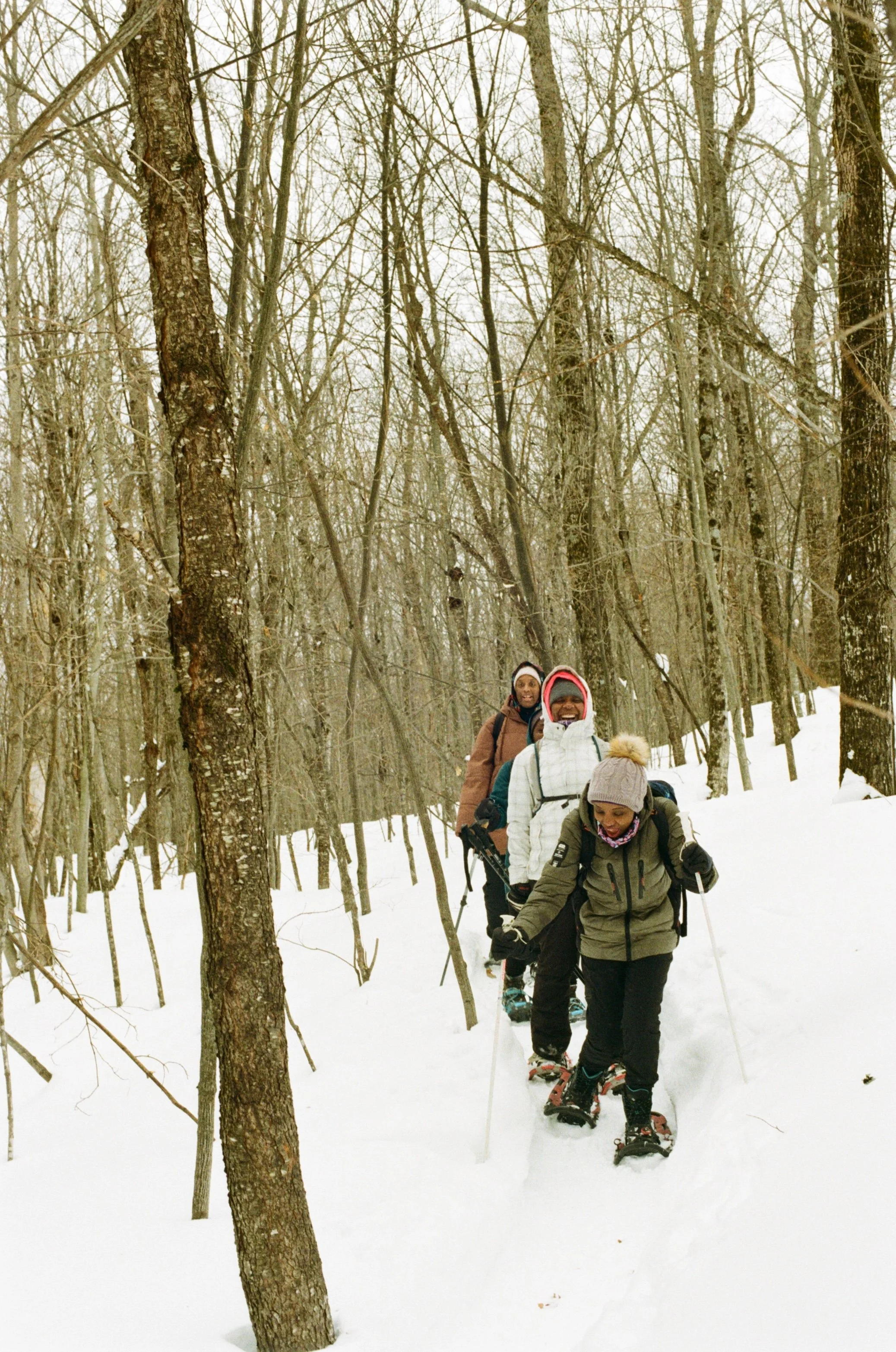 Group of five people hiking in a snowy forest, wearing winter clothing and snowshoes.