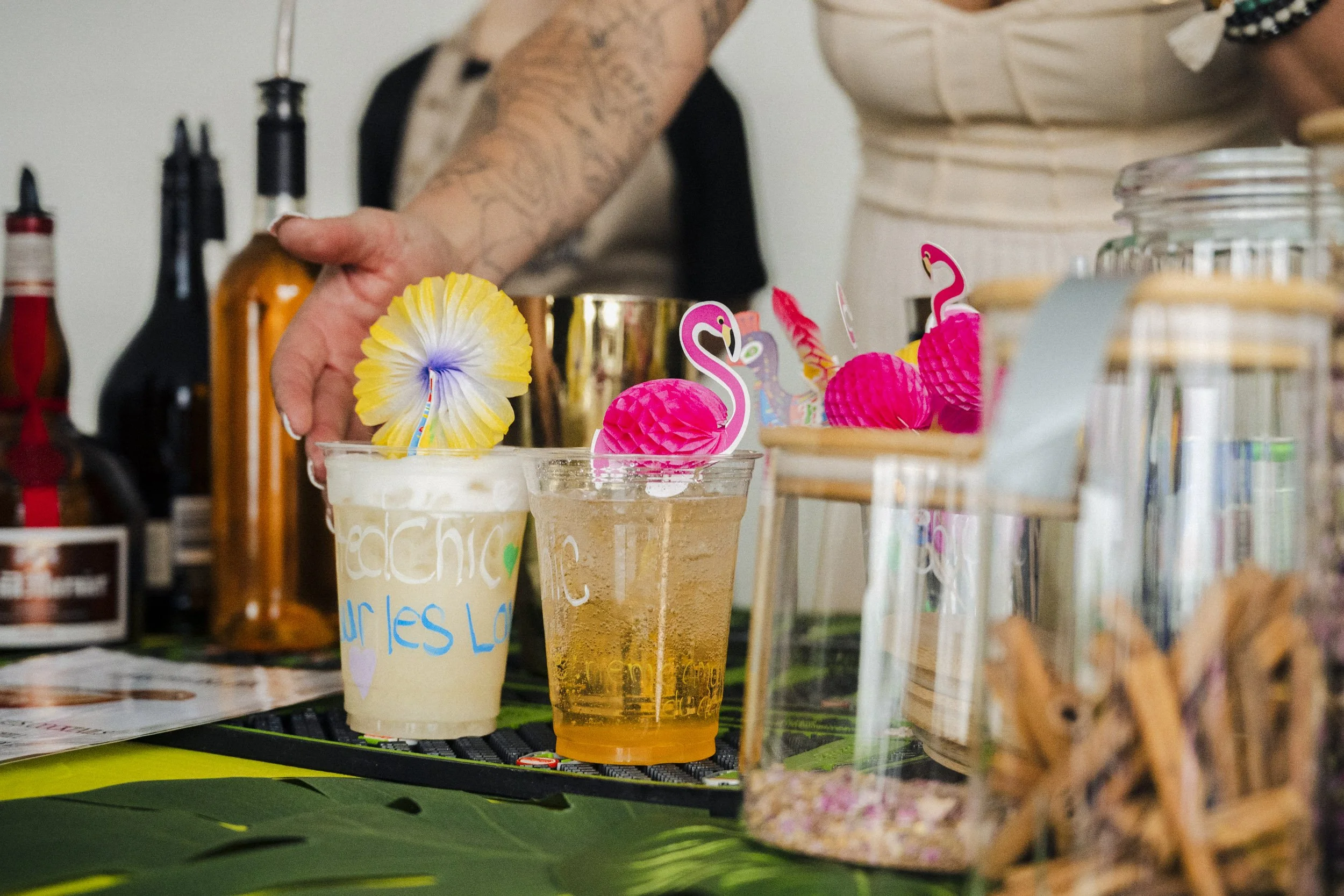 Close-up of colorful tropical-themed drinks with paper umbrellas, on a decorated table at a festive event.