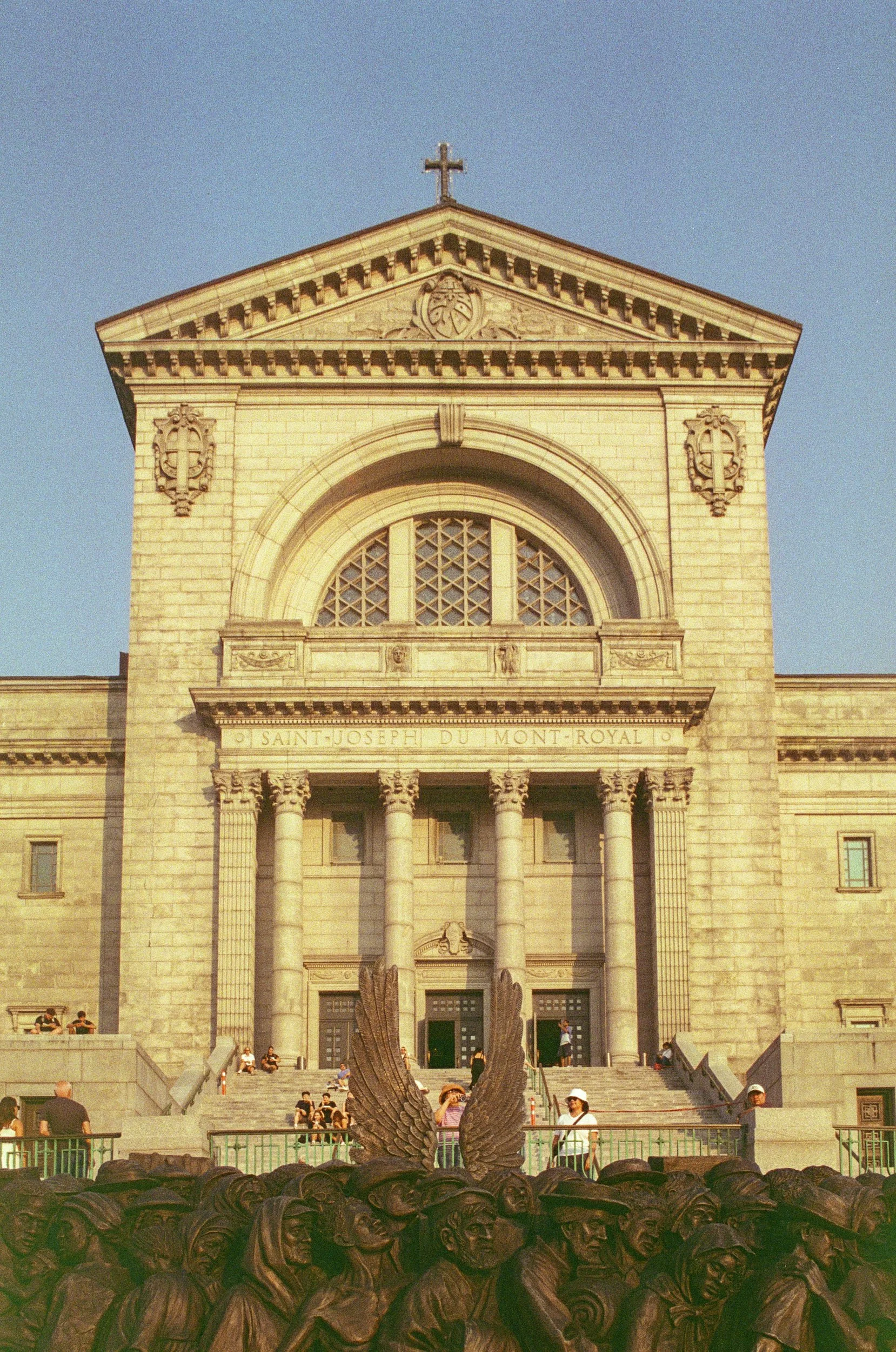 A bronze sculpture of soldiers in a circle in front of a large historic church or cathedral with steps and people sitting and walking.