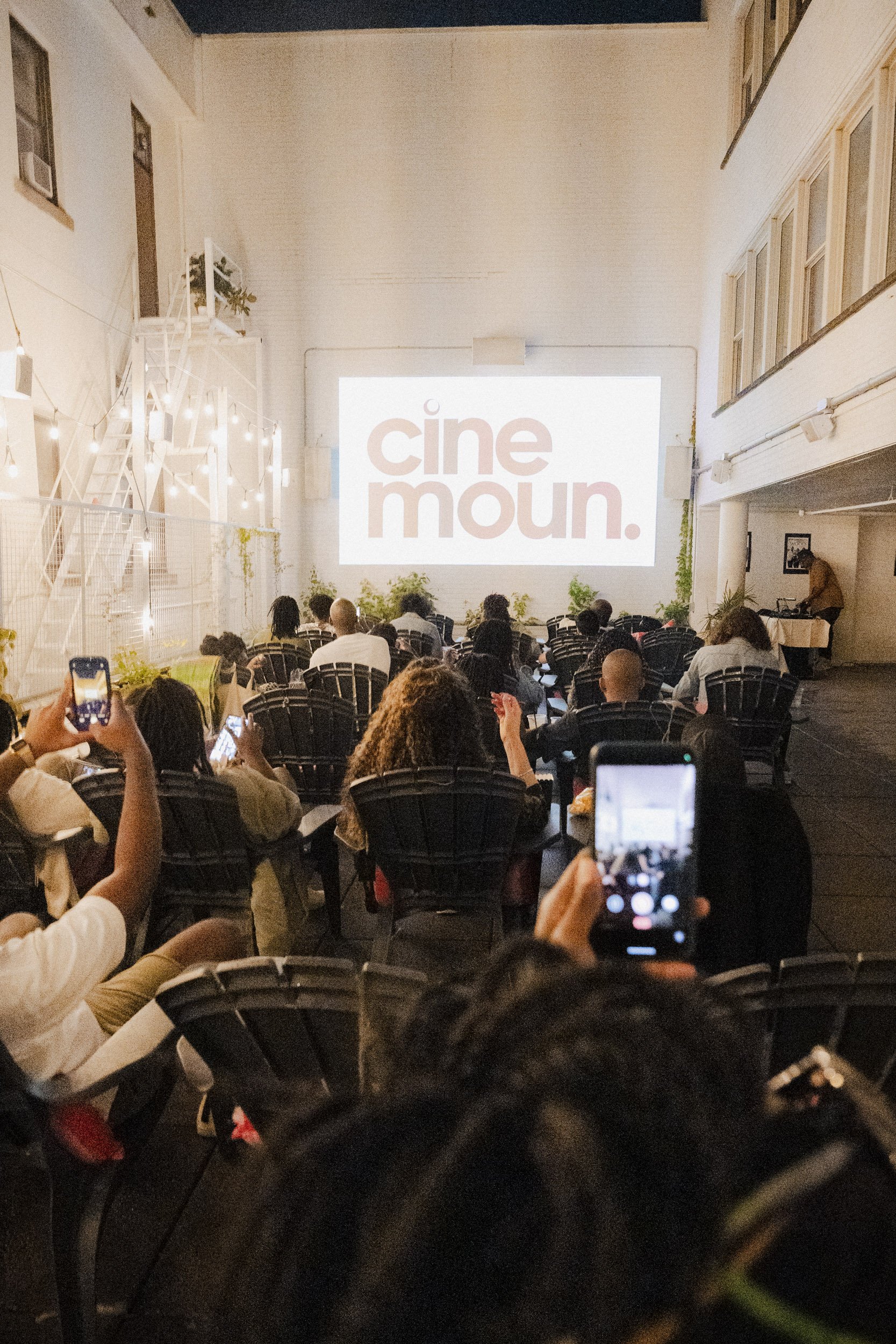 People seated and watching a presentation projected on a large screen with the words 'cine moud.' in a dimly lit room.