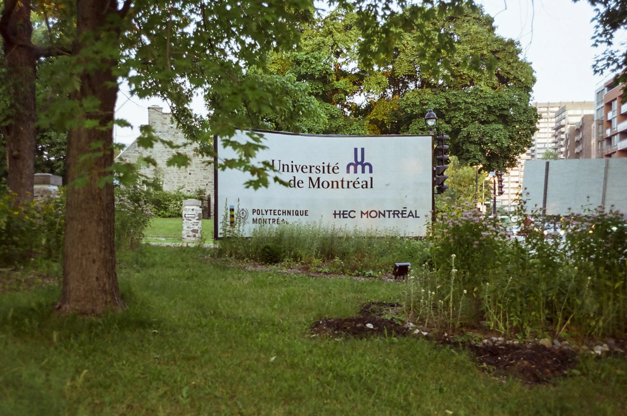 Sign on a university campus with trees and buildings in the background. The sign reads "Université de Montréal" with logos for Polytechnique Montréal and HEC Montréal.