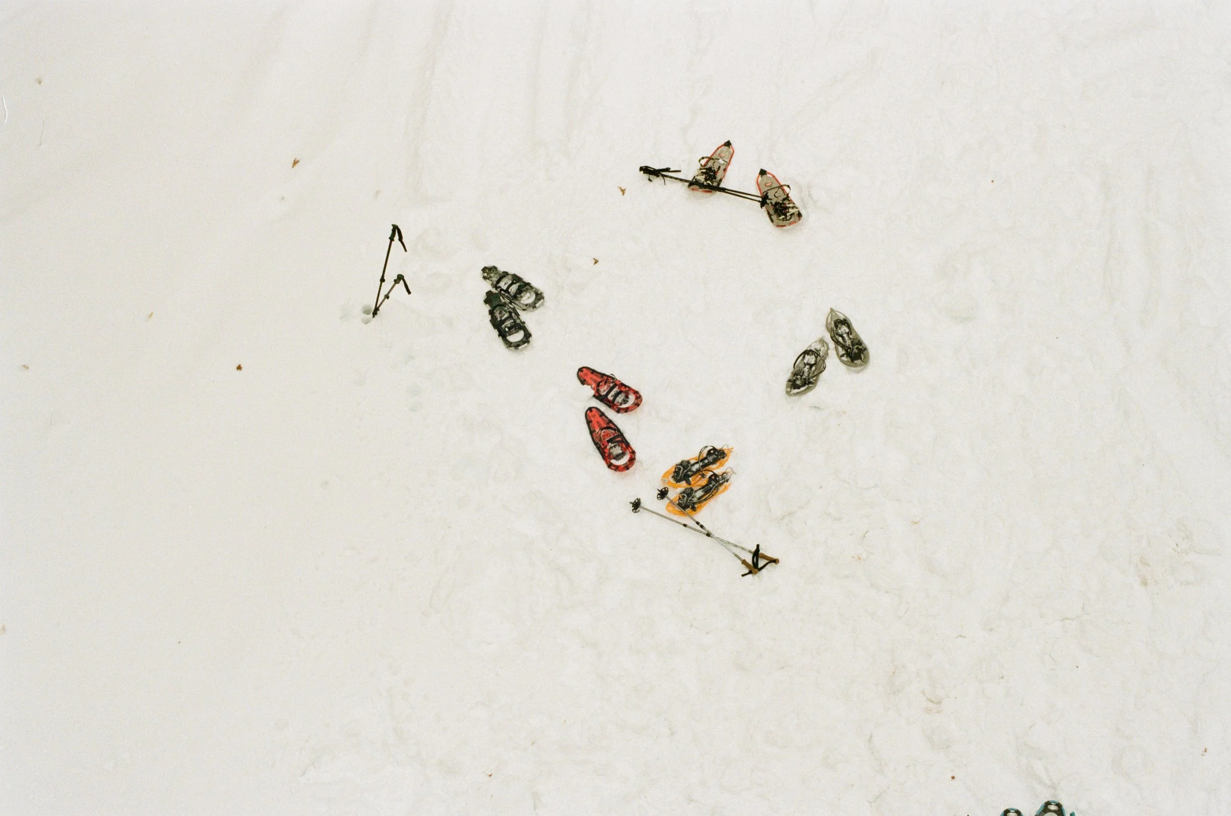 Ski equipment arranged on snow, including pairs of skis, ski poles, boots, and other gear.