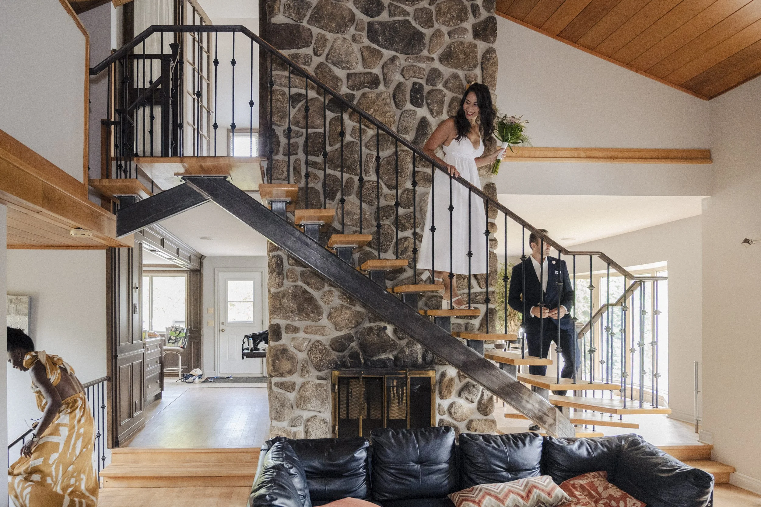 A woman in a white dress holding a bouquet of flowers standing on a staircase inside a house.