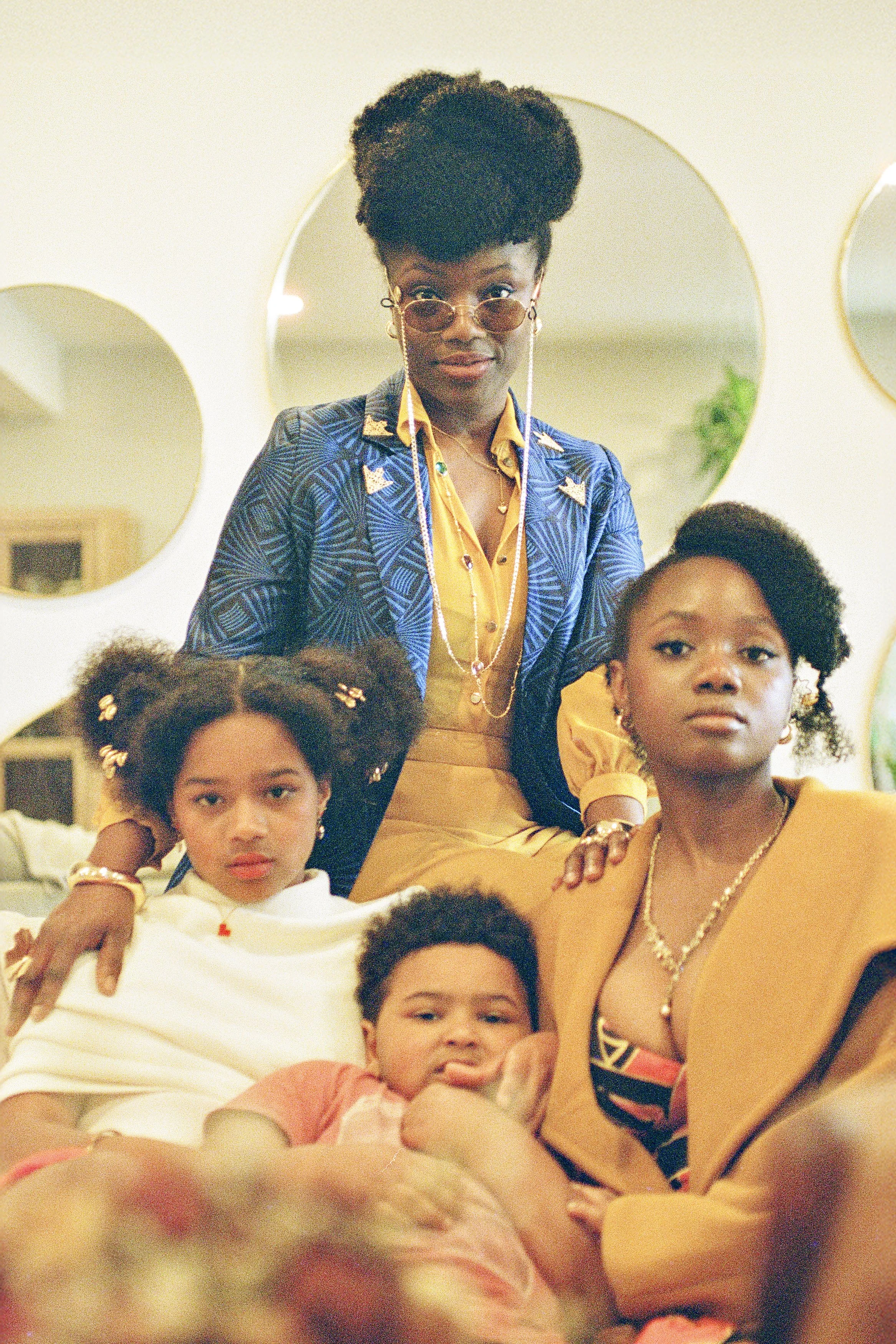 A woman wearing sunglasses and a blue patterned blazer poses with children in a social setting.