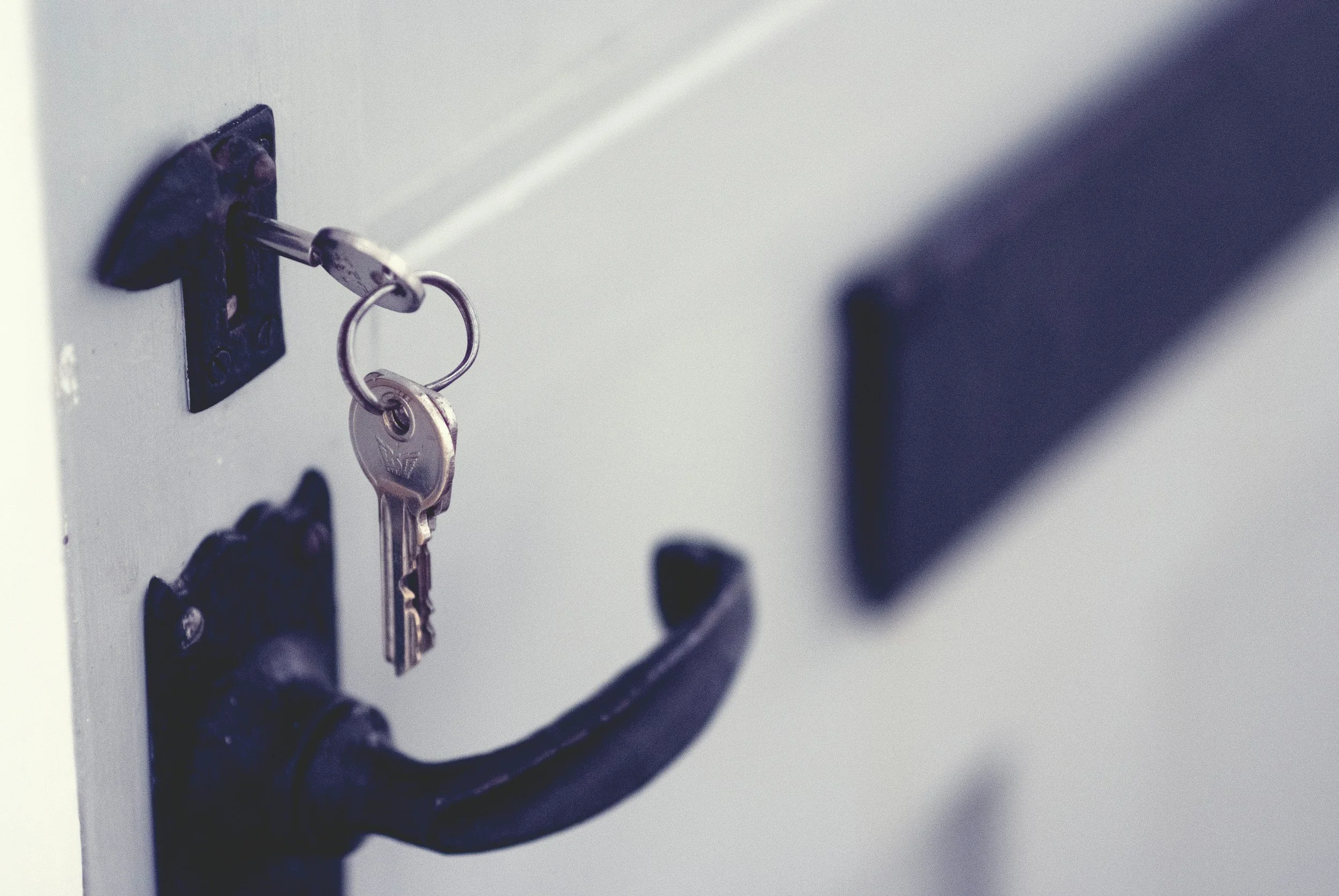 Close-up of a key inserted into a combination lock on a locker. The lock is black, and there are other keys hanging from it on a keyring. The locker is light gray.