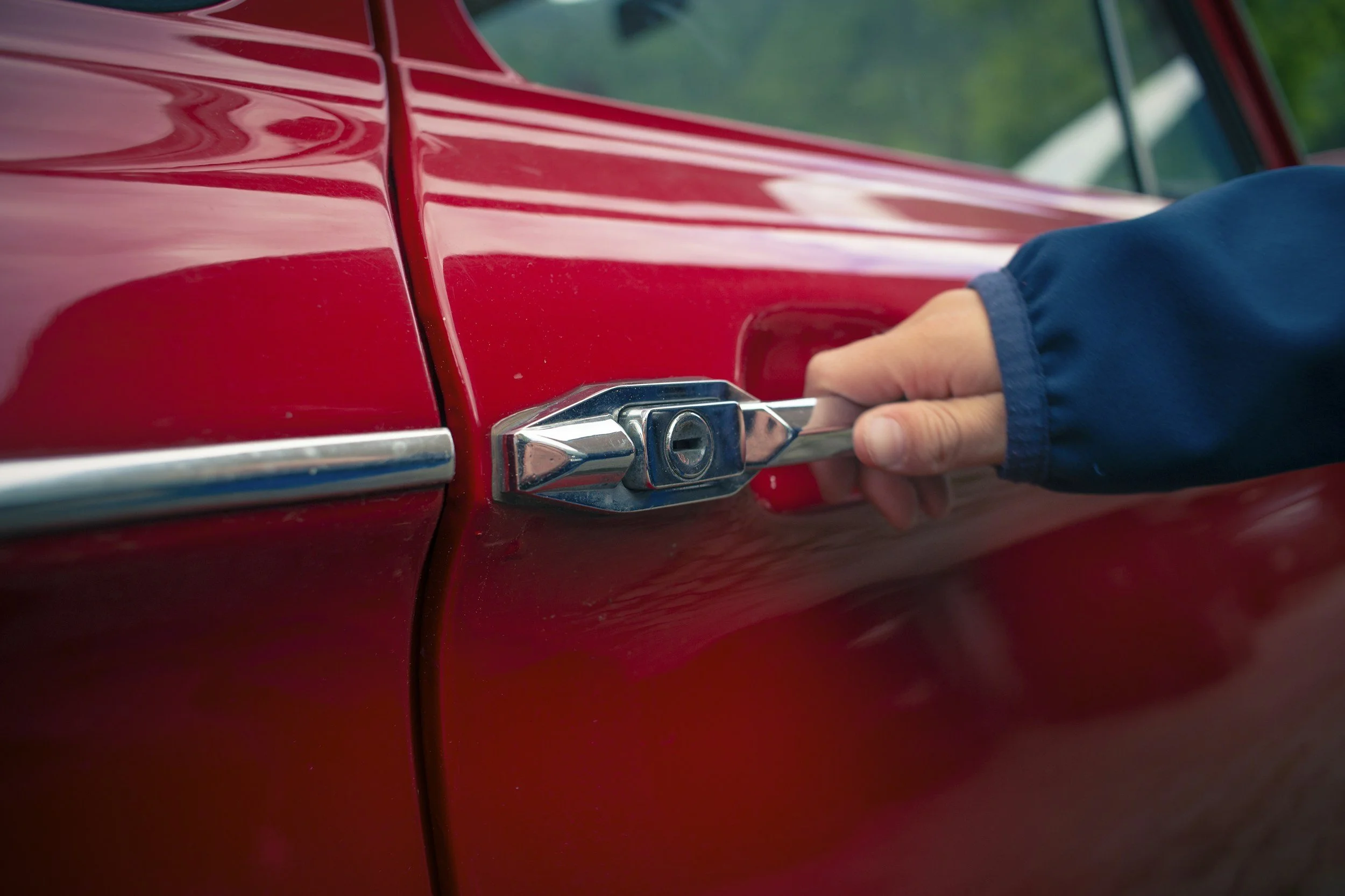 Close-up of a person locking a red vintage car using a key.