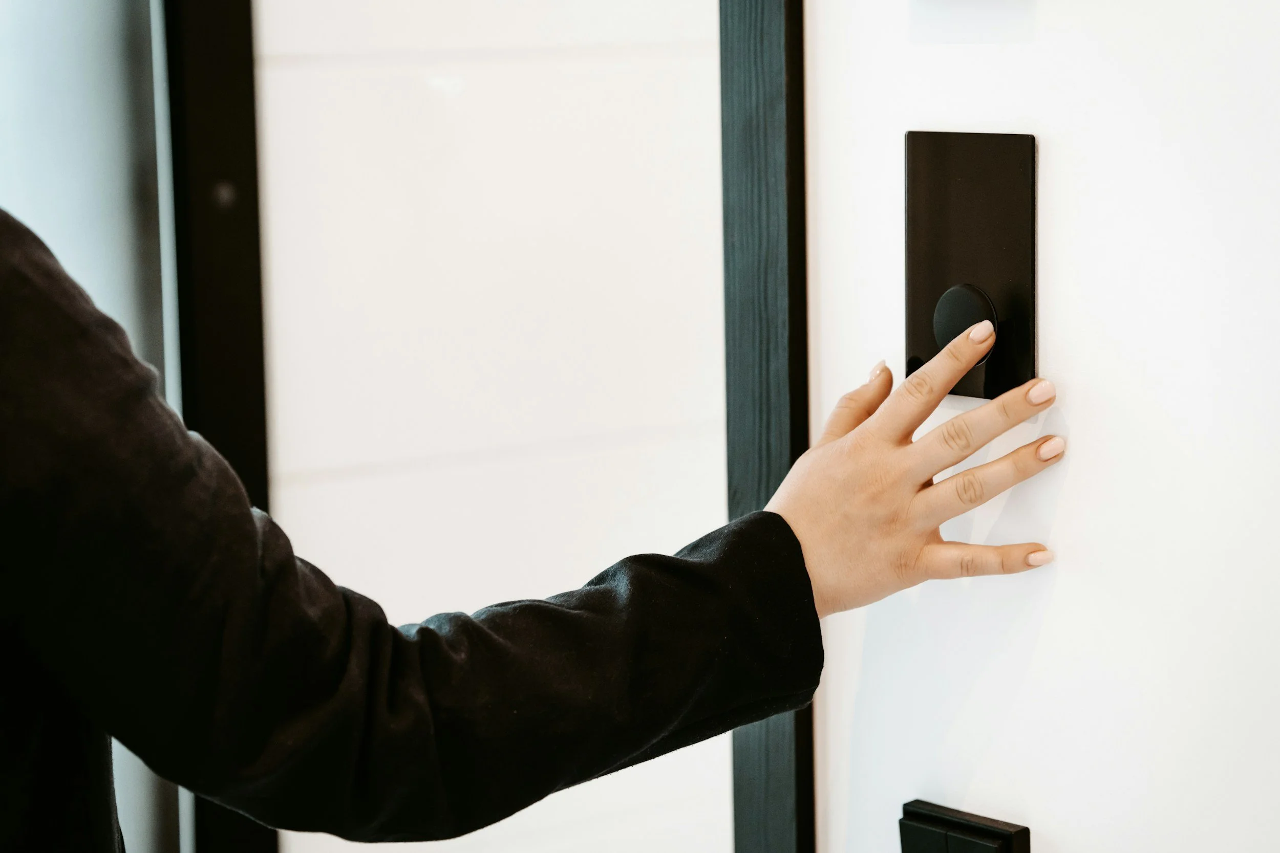 A person pressing a button on a black control panel or switch on a white wall.