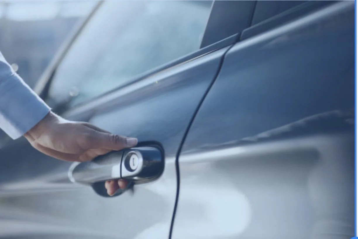 Close-up of a person unlocking a gray car door with a keyless entry remote.