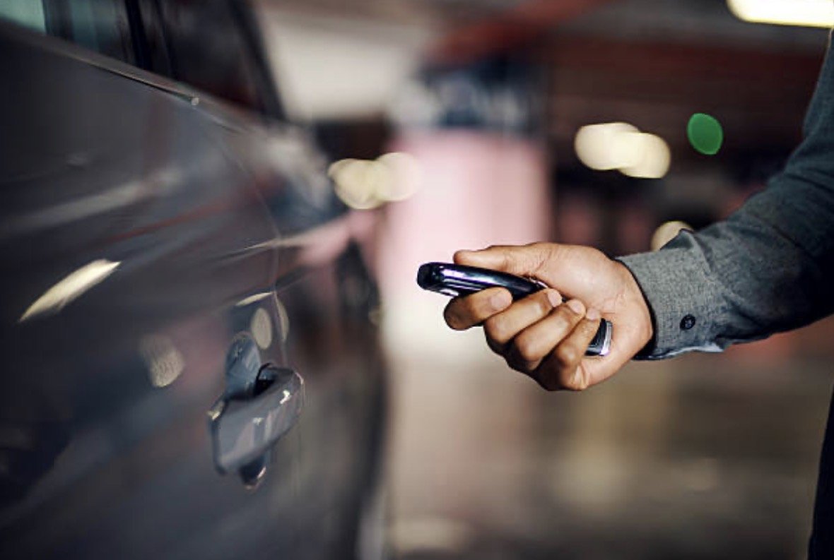 Person in gray suit using a smartphone near a black car in a parking garage.