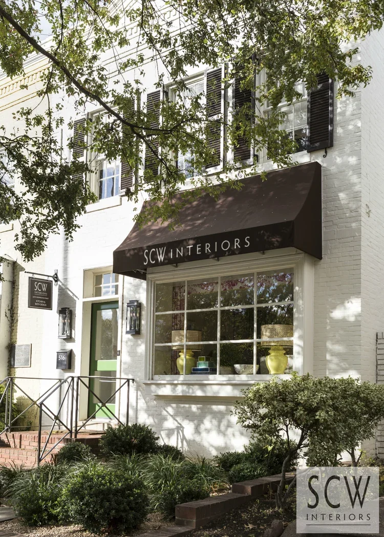 Exterior view of the SCW Interiors storefront featuring a white brick facade, black awning, large display window, and green front door.