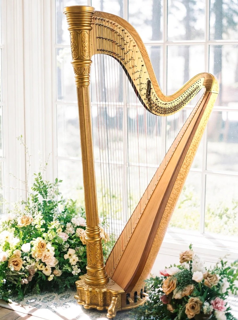 Gold concert harp surrounded by flowers in a bright wedding setting