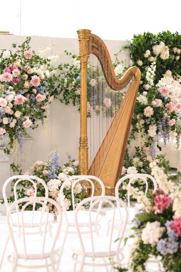 Gold concert harp surrounded by pastel wedding flowers in a bright ceremony room