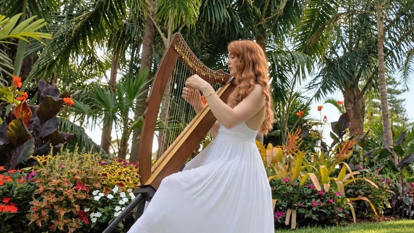 Jessica Holmlund playing her brown lap harp in a tropical garden