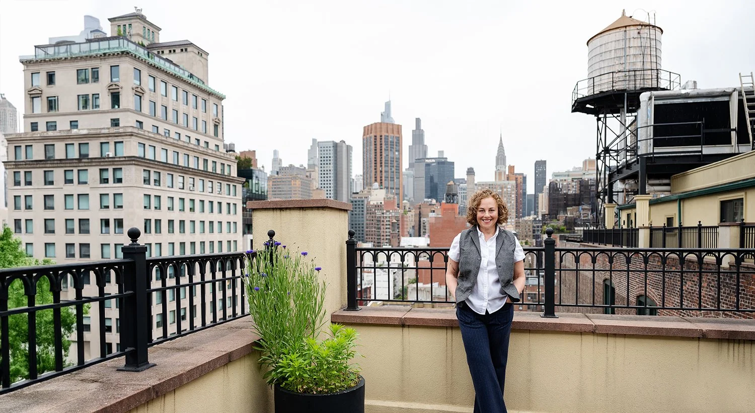 Carrie L. Jabinsky LCSW, JD Relational Therapist in New York City and Connecticut offering Integrative Psychotherapy for Individuals, Couples, and Families standing on a New York City rooftop terrace with a view of the New York City skyline, smiling.