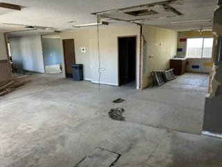 Empty room with damaged ceiling and floor, debris, and construction materials.