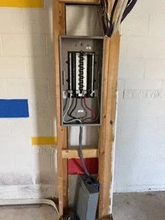 Open electrical breaker panel on a wooden wall with wiring inside.