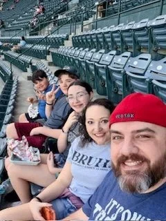 Youth director in stadium seats, smiling, with some food and drinks in front of them.