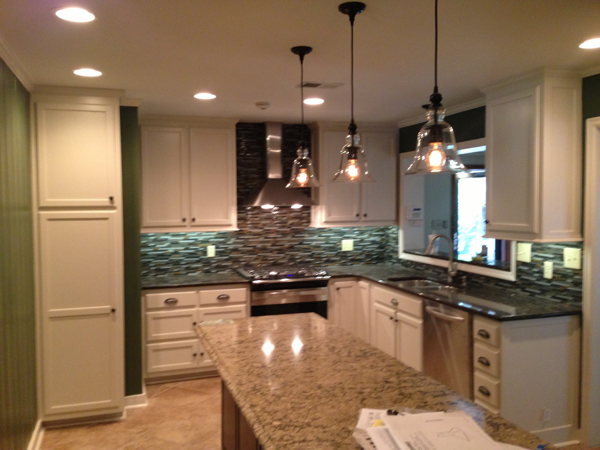 Kitchen with white cabinets, granite countertops, a mosaic tile backsplash, pendant lights, and a window.