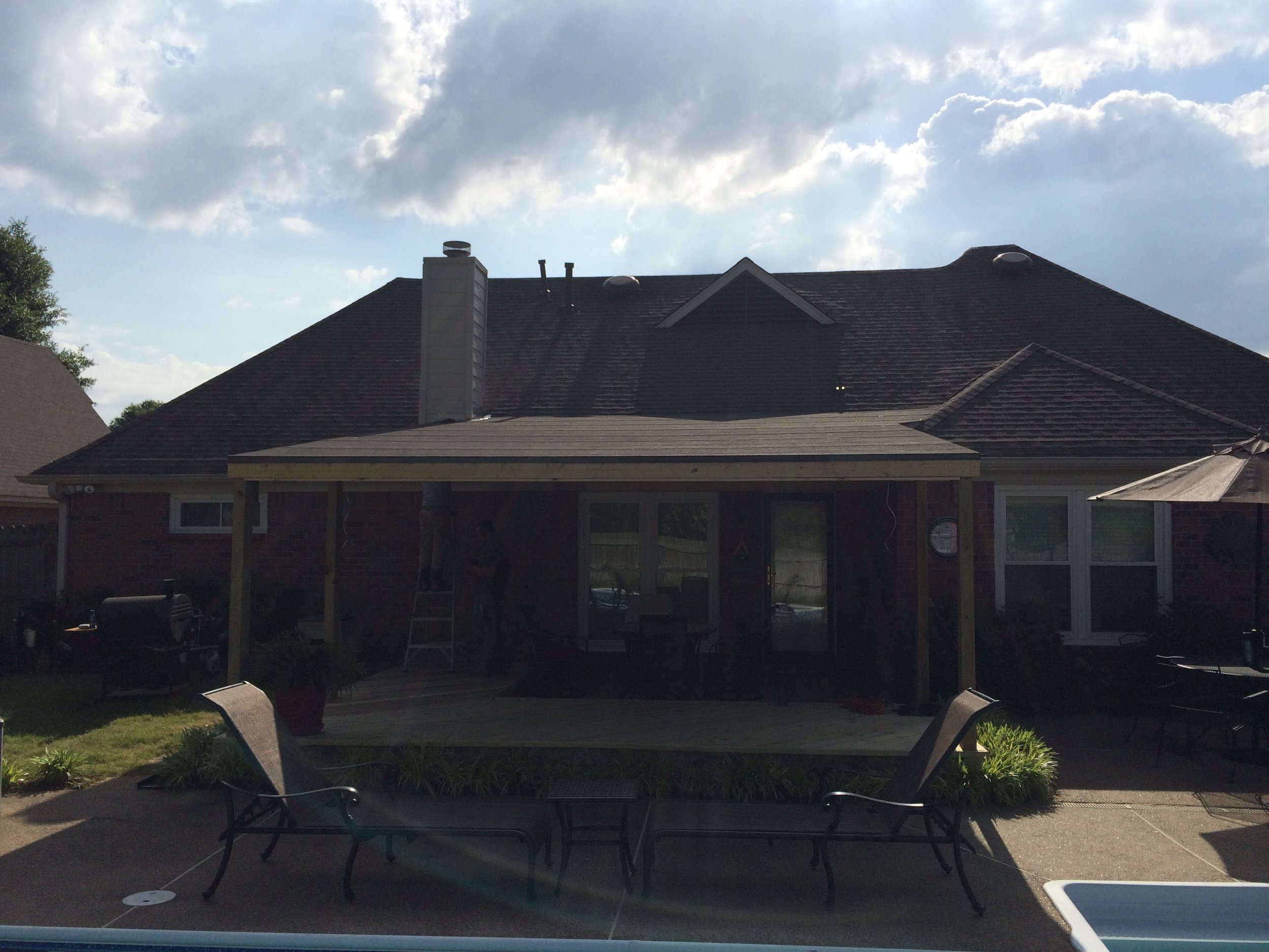 Photo of a backyard patio with a table and chairs, a covered back porch, a brick house with a chimney, and an overcast sky.